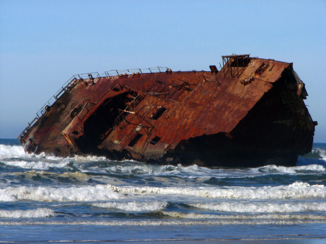 Large rusted ship wrecked on its side in the middle of the water.