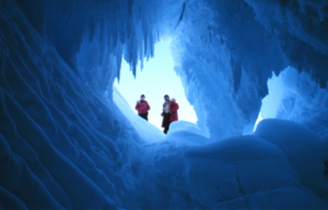 Two people stand at the top of an opening, photo taken from inside an ice cave in Antarctica.