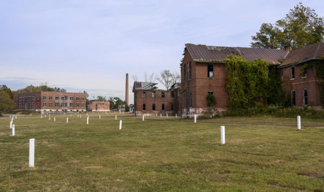 A field of graves, abandoned buildings in the background.