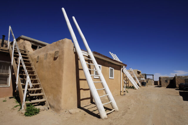 A adobe house with a big white ladder up its wall.