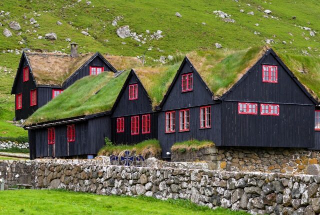 A black farmhouse with red trim and a grassy roof.
