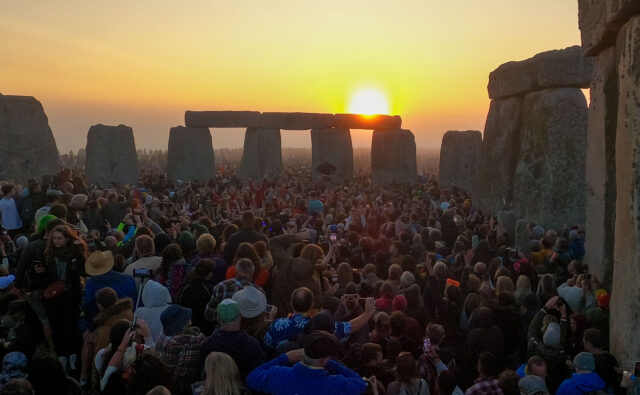 A large group of people gathered at Stonehenge at dusk.