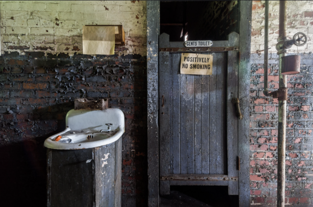 An abandoned sink beside the stall of a toilet.