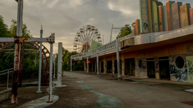 Pathway surrounded by abandoned buildings, with a Ferris wheel in the background