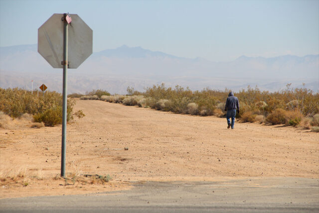 Man walking past a stop sign along a desert road